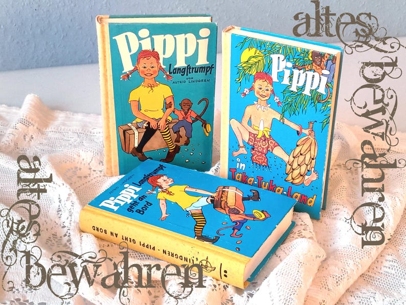 May include: Three vintage children's books with colorful illustrations of Pippi Longstocking. The books have blue covers with images of Pippi and text in German. The books are arranged on a white lace surface.