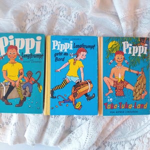 May include: Three vintage children's books with blue covers featuring illustrations of Pippi Longstocking. The books have yellow spines and depict Pippi in various adventures, with text in German. The covers feature vibrant colors and cartoon-style artwork.