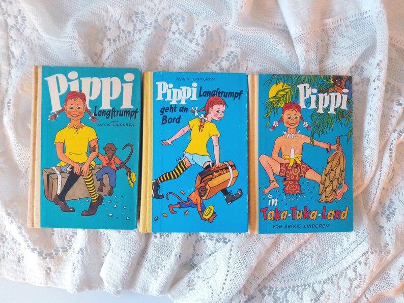 May include: Three vintage children's books with blue covers featuring illustrations of Pippi Longstocking. The books have yellow spines and depict Pippi in various adventures, with text in German. The covers feature vibrant colors and cartoon-style artwork.