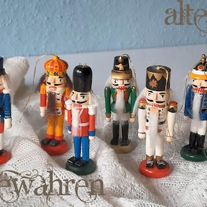 Könnte beinhalten: Sechs Holzfiguren, die Nussknacker darstellen, jeweils mit unterschiedlichen Uniformen und kleinen, runden Sockeln. Die Figuren haben weiße Haare und Schnurrbärte. Der Text "bewahren" ist sichtbar.