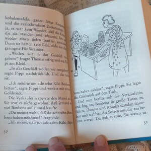 May include: Open book with text and a black and white illustration of a girl and a woman behind a counter. The text is in German. The book has a blue cover.