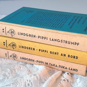 May include: Three vintage books stacked, featuring titles in German. The top book has a teal cover, while the others have cream and yellow spines. The titles include "Pippi Langstrumpf" and "Pippi Geht An Bord."