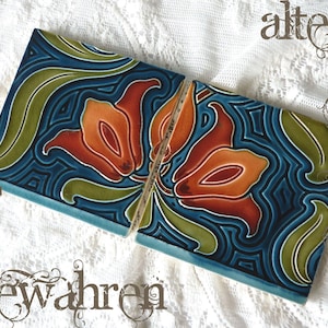 Może przedstawiać: Dwie ceramiczne płytki z kwiatowym wzorem. Płytki są w kolorze ciemnoniebieskim z pomarańczowymi i czerwonymi kwiatami oraz zielonymi liśćmi. Płytki są oddzielone cienkim kawałkiem drewna. Napis "altes bewahren" jest napisany ozdobną czcionką.