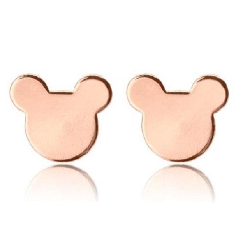 Pode incluir: Um par de brincos de bot&atilde;o em ouro rosa em forma de cabe&ccedil;a de rato. Os brincos t&ecirc;m um acabamento liso e polido e um design minimalista. S&atilde;o apresentados sobre um fundo branco.