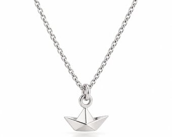 May include: A silver-toned necklace featuring a delicate chain and a small, three-dimensional pendant shaped like a folded paper boat. The pendant is suspended from a circular jump ring, showcasing clean, geometric lines and a polished metallic finish.