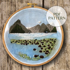 May include: Embroidered hoop art featuring a landscape scene with mountains, water, and rocks. The mountains are green and gray, the water is blue, and the rocks are brown. The hoop is made of wood and has a natural finish.