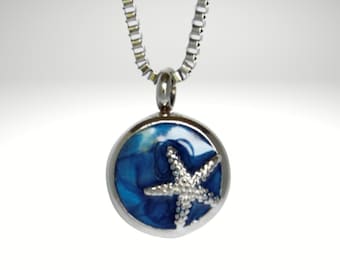 Può includere: Una collana con catena d'argento con un ciondolo rotondo che presenta un design a conchiglia blu e bianca con una stella marina argentata in cima.