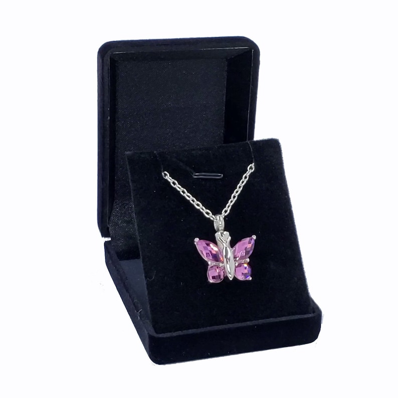 May include: A pink butterfly pendant necklace in a black velvet jewelry box.