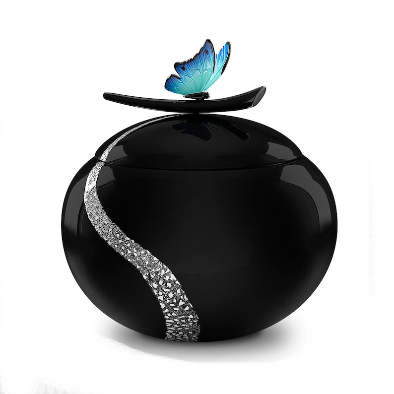 Puede incluir: Jarr&oacute;n de cer&aacute;mica negro con un dise&ntilde;o de espiral plateado y una mariposa azul en la tapa.