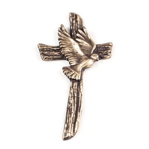 May include: A bronze-toned metal cross featuring a textured, wood-grain appearance. A sculpted dove with outstretched wings is positioned in the center of the cross, appearing to fly upward. The entire piece has a metallic finish with dark highlights.