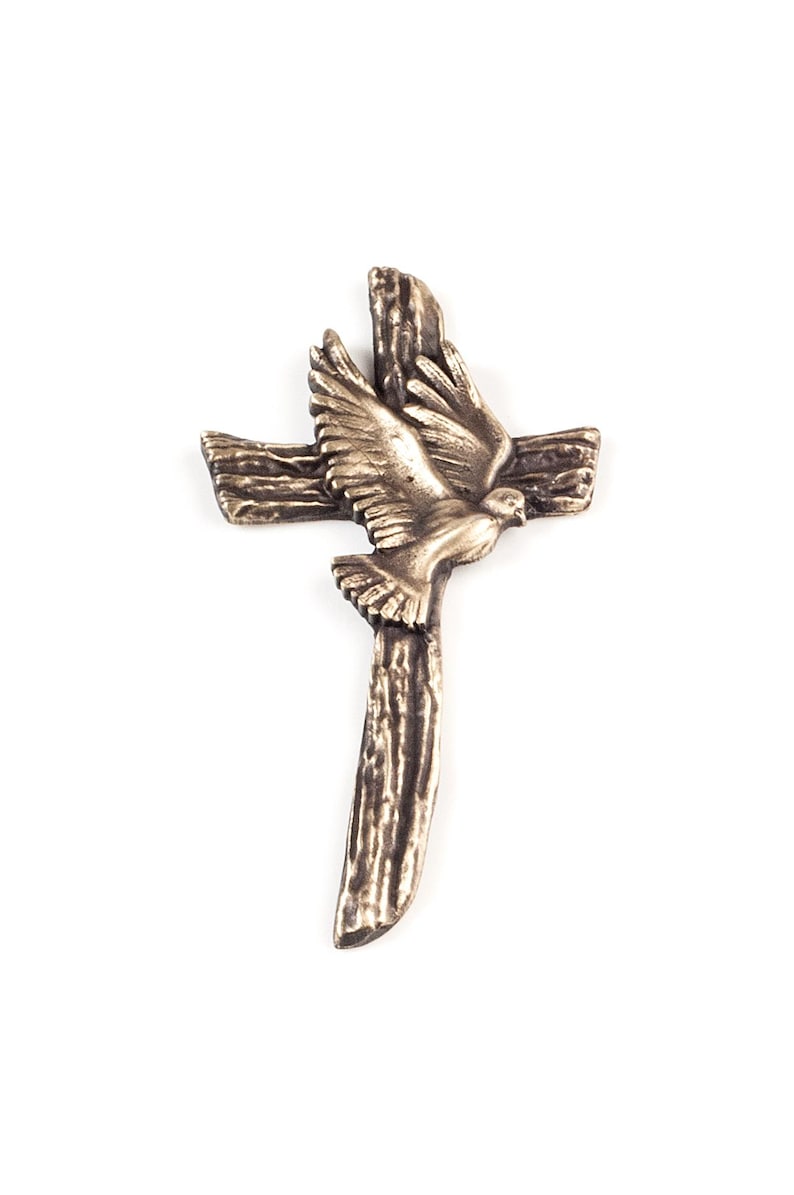 May include: A bronze-toned metal cross featuring a textured, wood-grain appearance. A sculpted dove with outstretched wings is positioned in the center of the cross, appearing to fly upward. The entire piece has a metallic finish with dark highlights.