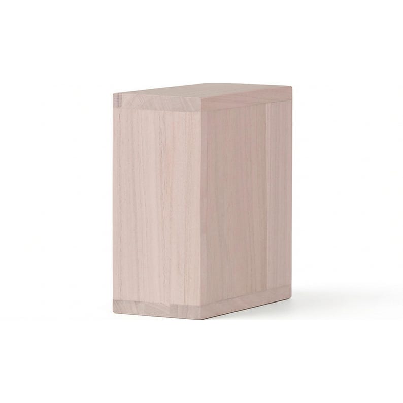May include: A light-colored, rectangular wooden box with a slightly angled top. The box is made of light-colored wood and has visible wood grain. The box is a simple, minimalist design.