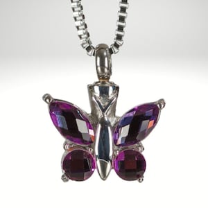 May include: A silver chain necklace with a purple butterfly pendant. The butterfly has faceted crystal wings and a silver body.