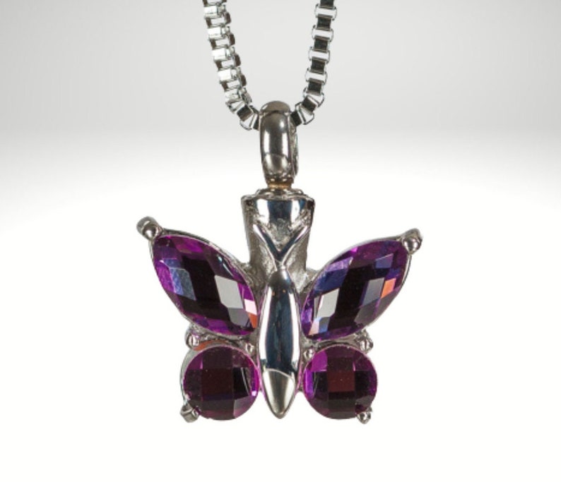 May include: A silver chain necklace with a purple butterfly pendant. The butterfly has faceted crystal wings and a silver body.