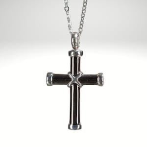 May include: A silver cross pendant necklace with a black cross. The cross has a detailed design with a small cross in the center.