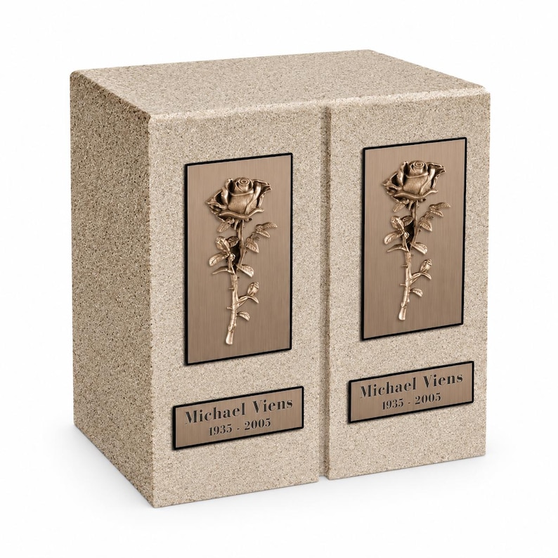 May include: A rectangular beige stone companion urn featuring two bronze-toned plaques, each displaying a raised rose relief. Below each rose, a rectangular bronze nameplate is engraved with the text Michael Viens 1935 - 2005 in black lettering.