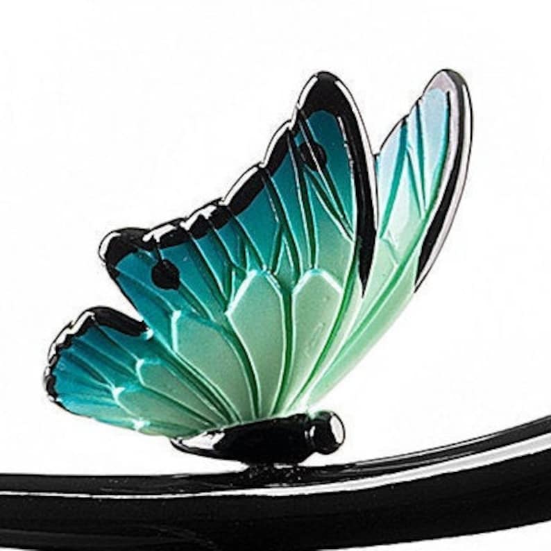May include: A black metal butterfly with teal and green wings. The butterfly is perched on a black metal branch.