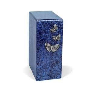 May include: A blue rectangular urn with a textured surface and three silver butterfly embellishments. The urn has a slightly angled top and a simple, elegant design. The butterflies are arranged vertically on the front of the urn.