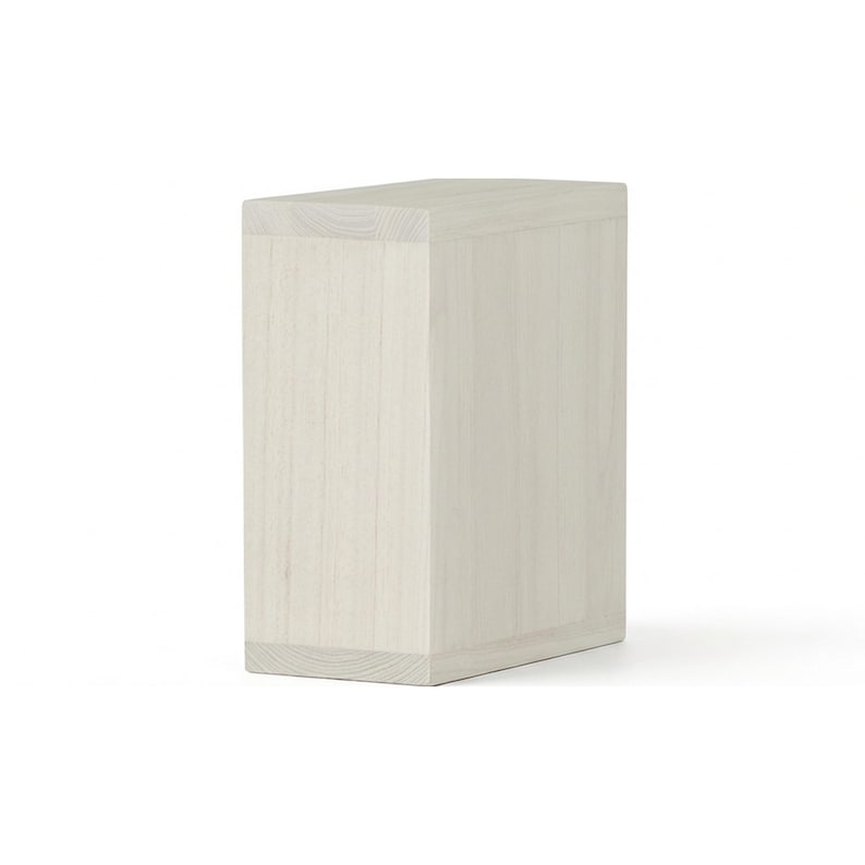 May include: A light-colored, rectangular wooden block with a slightly angled top. The wood grain is visible, and the block appears to be made of multiple pieces joined together. The overall design is simple and modern, suitable for various decorative or functional uses.