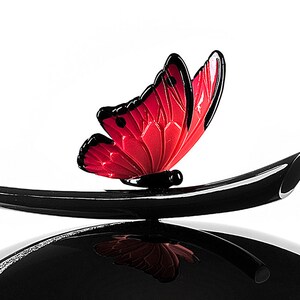 Puede incluir: Un adorno de mariposa de vidrio negro y rojo con un tallo negro. La mariposa tiene un cuerpo rojo y alas negras.