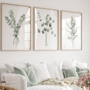 Watercolor set of 3 prints cosnisting of olive branch and eucalyptus against white background hangs in a modern living room. These watercolor plants are painted in sage green and delicate shades of green. Fine art posters available in all sizes.
