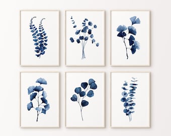 Puede incluir: Conjunto de seis impresiones de acuarela azul índigo con diversas ilustraciones botánicas de hojas y ramas. Las impresiones están enmarcadas en marcos simples de madera clara y están dispuestas en una cuadrícula en una pared blanca.