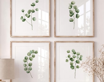 May include: A set of four square wall art prints featuring watercolor illustrations of green eucalyptus branches on a white background, each enclosed in a light wood frame and arranged in a two-by-two grid on a wall.