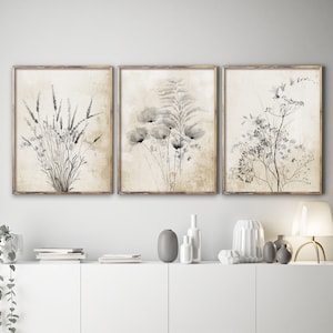 Modern vintage fine art posters depicting rustic black flowers on a vintage background hang in wooden frames in a modern living room, above a white drawer.