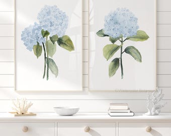 May include: Two framed vertical wall art prints featuring watercolor illustrations of light blue hydrangea flowers with green leaves on a white background. The text Watercolor Botanicals is visible in the bottom right corner of the right print.