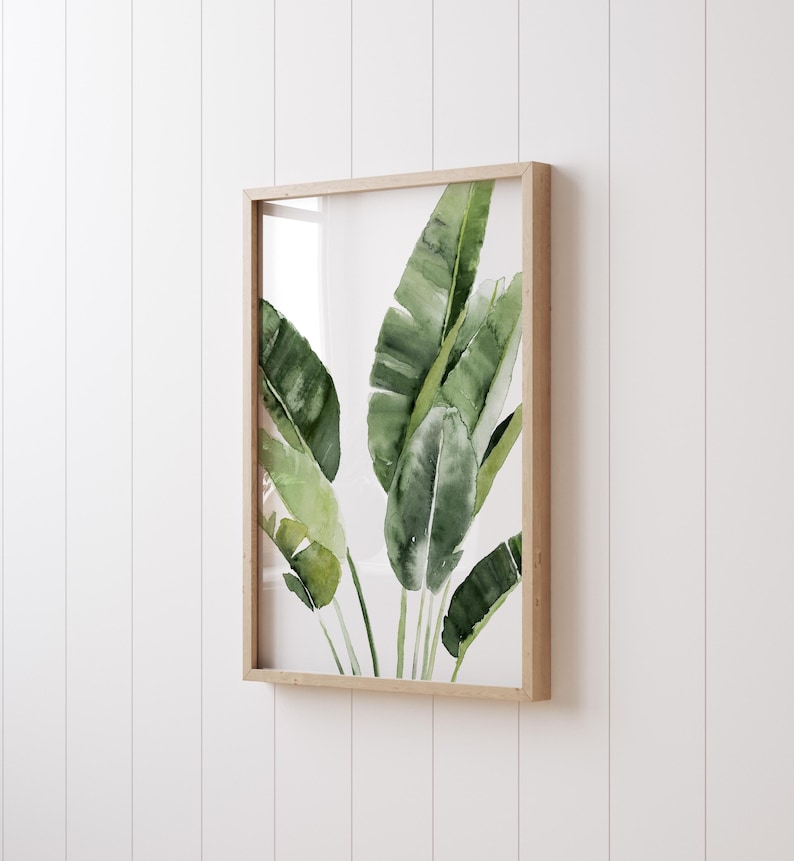 A framed watercolor painting of green banana leaves on a white background.