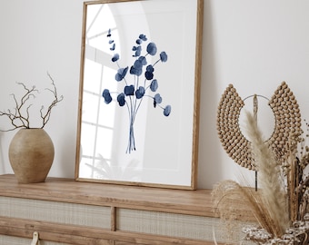Puede incluir: Una impresión artística enmarcada con una ilustración en acuarela de un ramo de hojas de eucalipto azules. La obra de arte se exhibe sobre un mueble de madera con un diseño de ratán tejido. También se ven objetos decorativos.