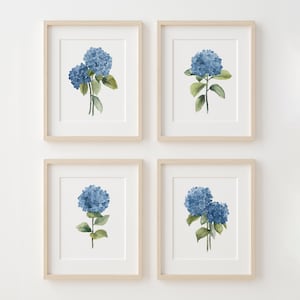 以下が含まれることがあります： ミニマルなスタイルで描かれた青いアジサイの水彩画4枚セット。それぞれのプリントは、白い背景に繊細な緑の葉をつけたアジサイの花を1輪ずつ描いています。