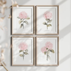 May include: Set of four watercolor prints featuring pink hydrangeas with green leaves. The prints are framed in light wood frames and are displayed on a white wall.