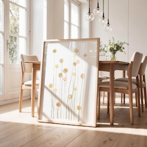 May include: A framed watercolor painting of a field of yellow and orange flowers with green stems. The painting is hanging on a wall in a dining room with a wooden table and chairs.