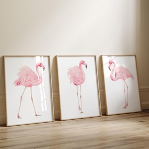 Puede incluir: Tres cuadros de pared con ilustraciones en acuarela de flamencos rosas. Cada lámina muestra un flamenco en una pose diferente sobre un fondo blanco, enmarcados en madera de color claro.