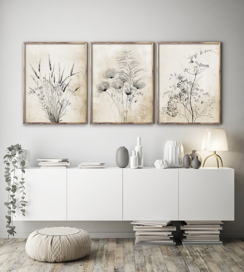 Modern vintage fine art posters depicting rustic black flowers on a vintage background hang in wooden frames in a modern living room, above a white drawer.