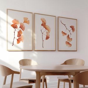 Könnte beinhalten: Drei gerahmte Aquarelldrucke von Ginkgoblättern in Orange- und Brauntönen. Die Drucke sind in einer Reihe an einer weißen Wand angeordnet.