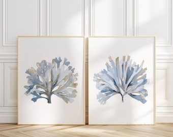May include: Two rectangular wall art prints featuring watercolor illustrations of sea coral in shades of dusty blue and muted beige. Each print is encased in a thin gold frame, showcasing organic, branching structures against a white background.