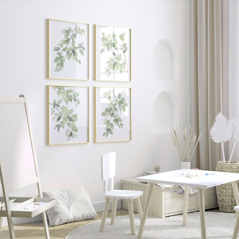 May include: A white wooden easel with a white board and a small drawer. A white wooden table and chair are in the foreground. Four framed prints with green watercolor leaves are on the wall.