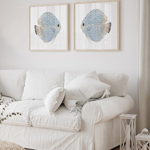 Minimalist coastal wall decor featuring watercolor blue fishes inserted into square frameshang above a white couch in a modern coastal living room.