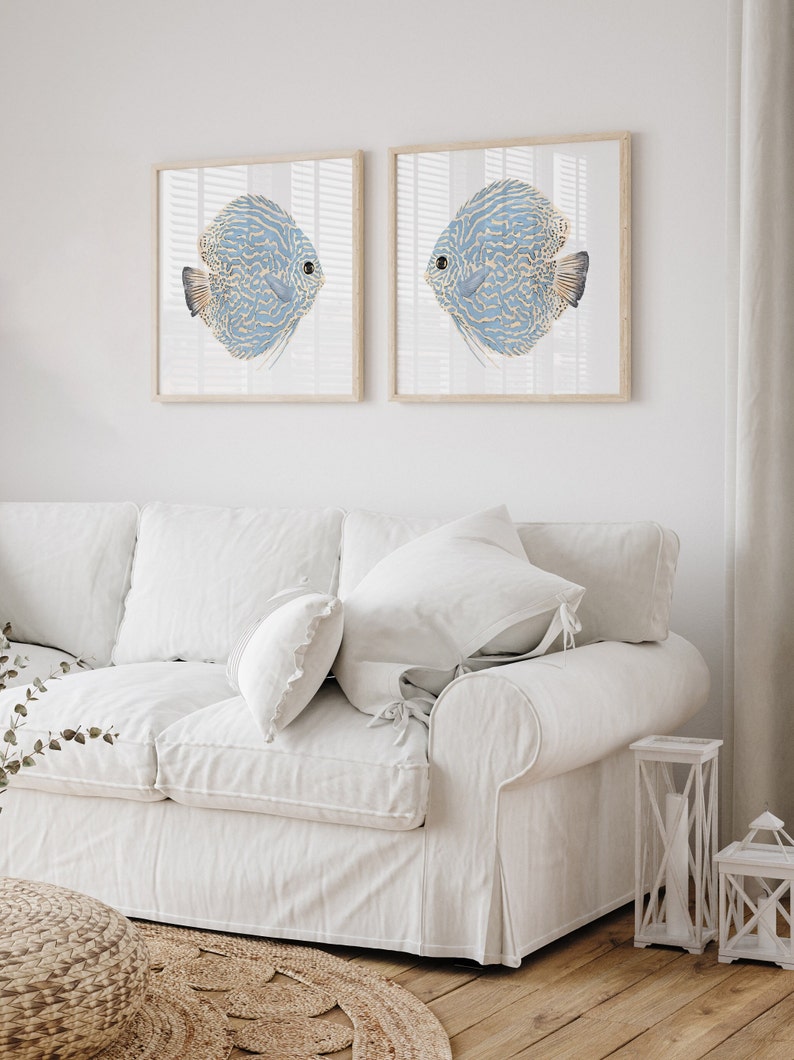 Minimalist coastal wall decor featuring watercolor blue fishes inserted into square frameshang above a white couch in a modern coastal living room.