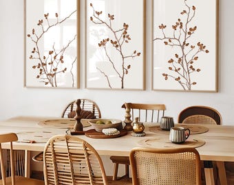 May include: A set of three framed wall art prints featuring brown botanical illustrations of rose hip branches on a light cream background, displayed in light wood frames above a wooden dining table with chairs.