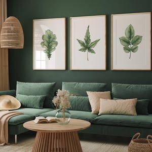 Peut inclure: Trois aquarelles encadrées de feuilles vertes sur un mur vert au-dessus d'un canapé d'angle avec un plaid et des coussins.