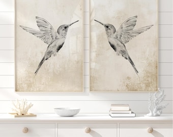 May include: Two framed prints of watercolor hummingbirds in flight against a beige background. The birds are facing opposite directions.