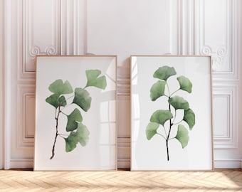 Puede incluir: Dos impresiones de acuarela enmarcadas de hojas verdes de ginkgo sobre un fondo blanco. Las impresiones están en marcos de madera simples y están colgadas en una pared blanca.