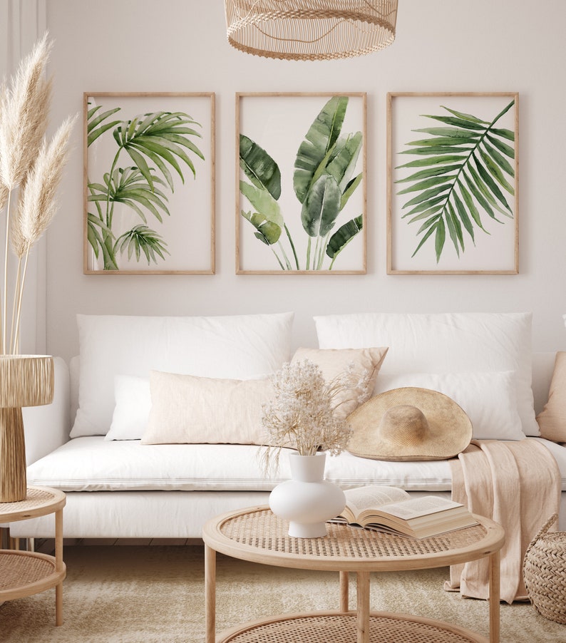 Vivid green tropical leaves on white background hang in wooden frames above a couch in a modern living room in a coastal boho style.