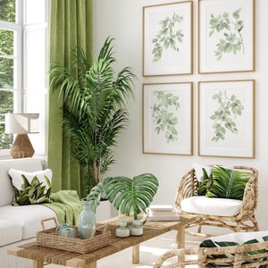 May include: A living room interior design with a white sofa, two wicker chairs with green leaf patterned cushions, a wooden coffee table with a woven tray, a large green potted plant, and four framed watercolor paintings of green leaves on the wall.