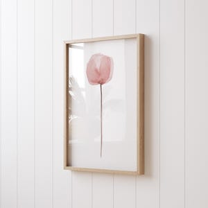 Può includere: Un dipinto ad acquerello incorniciato di un singolo fiore rosa con un lungo stelo su uno sfondo bianco.