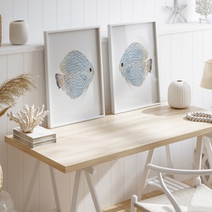 Minimalist beach house decor featuring watercolor blue fishes stands on a desk in white frames.