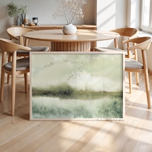 Könnte beinhalten: Ein gerahmter Landschaftskunstdruck mit einem weichen Aquarellverlauf in Salbeigrün, Oliv und Creme. Die Komposition zeigt eine neblige Horizontlinie mit einem Schwarm kleiner schwarzer Vögel, die in der oberen Bildmitte fliegen.